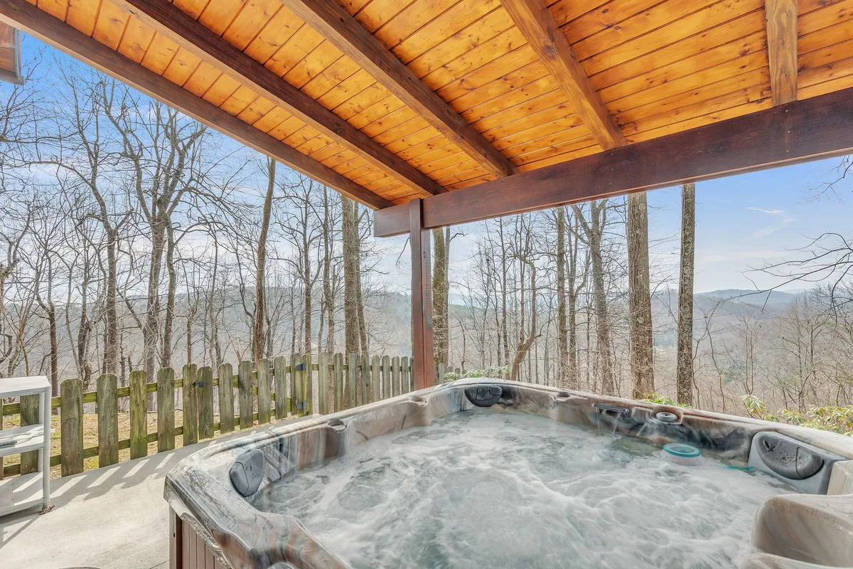 This exterior shot features a hot tub under a wooden ceiling, set against a natural landscape backdrop. The atmosphere is serene, and the image suggests unwinding in the hot tub while enjoying sunset views or stargazing at night.
