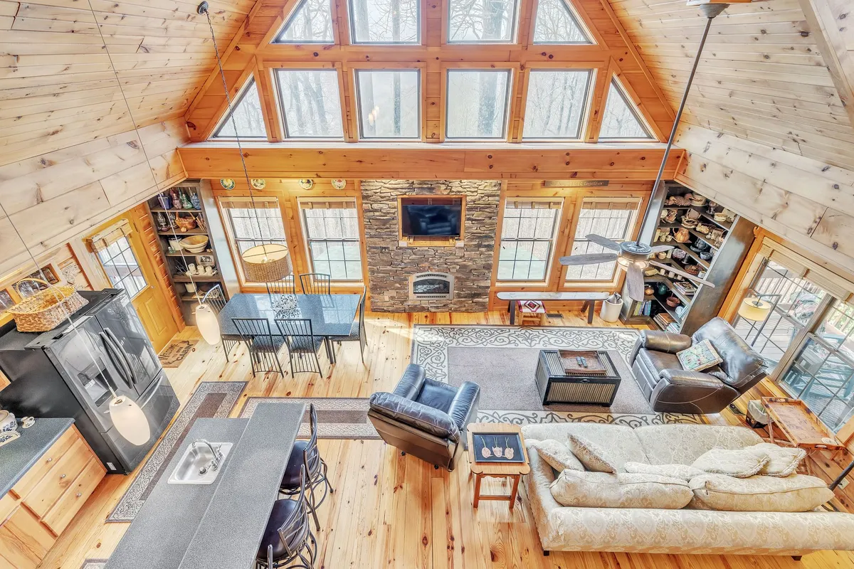 An expansive communal space featuring a dining area ideal for shared meals, a cozy sofa seating area beside a fireplace, kitchen island for casual gatherings, and large windows that provide glimpses of the outdoors.