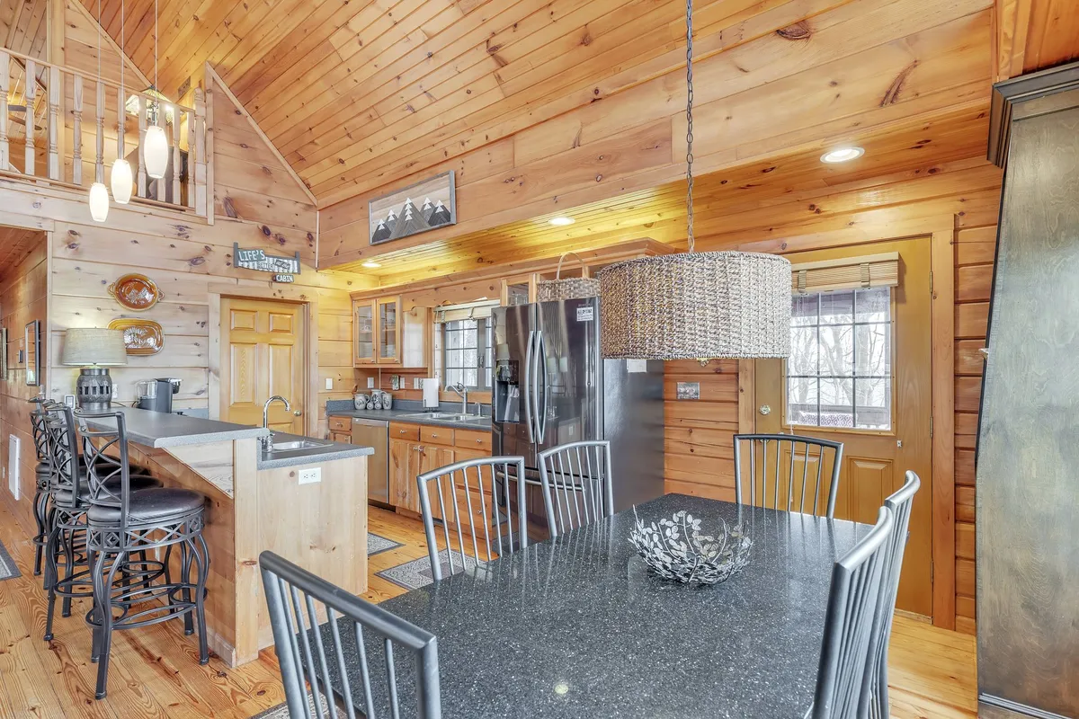A large dining area connected to a kitchen with wooden cabinetry, a high ceiling, stainless steel appliances, and a welcoming dining table perfect for shared meals. The space is airy and open, encouraging gatherings and conversation.
