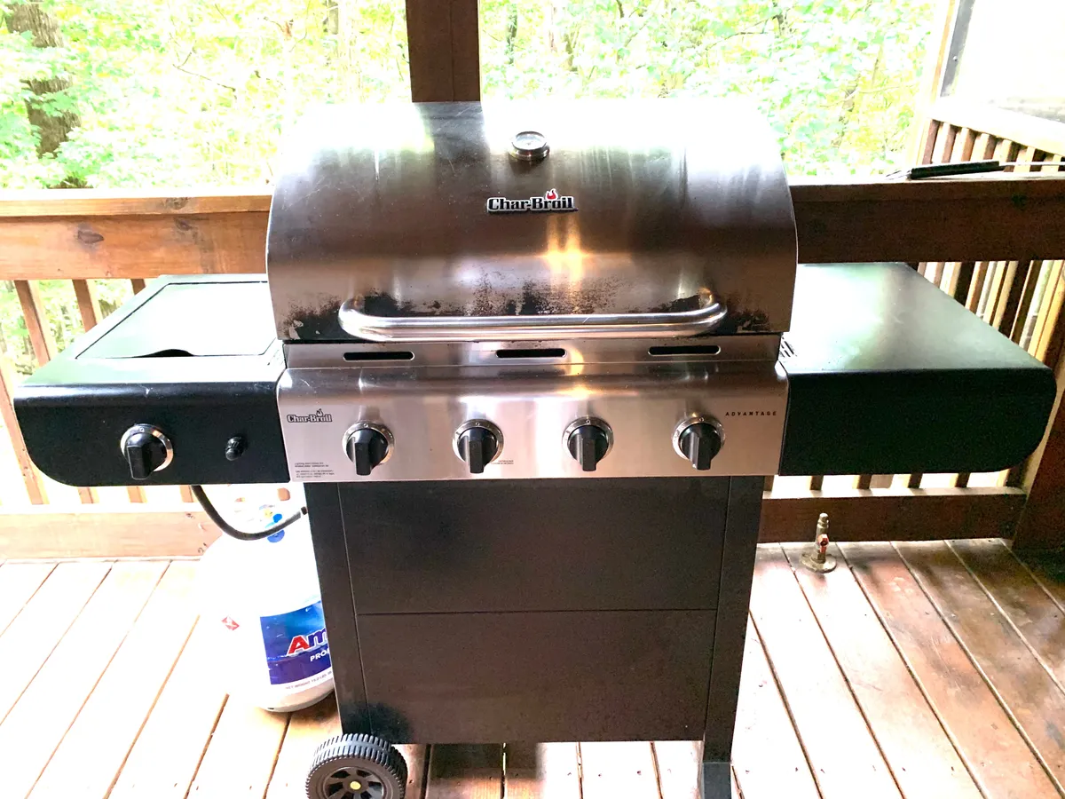 An inviting outdoor grill area on a wooden deck, featuring a propane grill and surrounded by nature. The space is set up for barbecuing and social gatherings, blending indoor and outdoor culinary experiences.