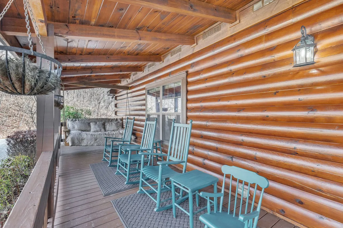 A welcoming front porch featuring classic rocking chairs, a charming porch swing, exposed wooden logs, and a hanging planter by the entryway. The scene radiates warmth and relaxation, inviting guests to sit, unwind, or socialize while enjoying the tranquil outdoor setting.