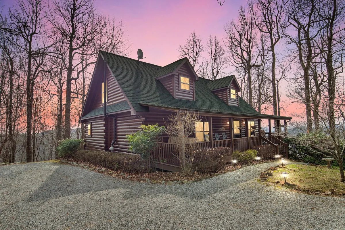 The hero image showcases a charming luxury log cabin nestled among tall trees in the Blue Ridge Mountains. The spacious front porch, complete with classic rocking chairs, invites guests to relax and take in the tranquil natural surroundings. The scene radiates warmth and serenity, making it ideal for both intimate getaways and group gatherings.