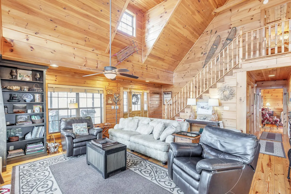 A large, inviting sectional sofa anchors a comfortable living area, complemented by black armchairs, a decorative bookshelf, a wooden staircase, and natural light—ideal for socializing, playing games, or unwinding after a day out.