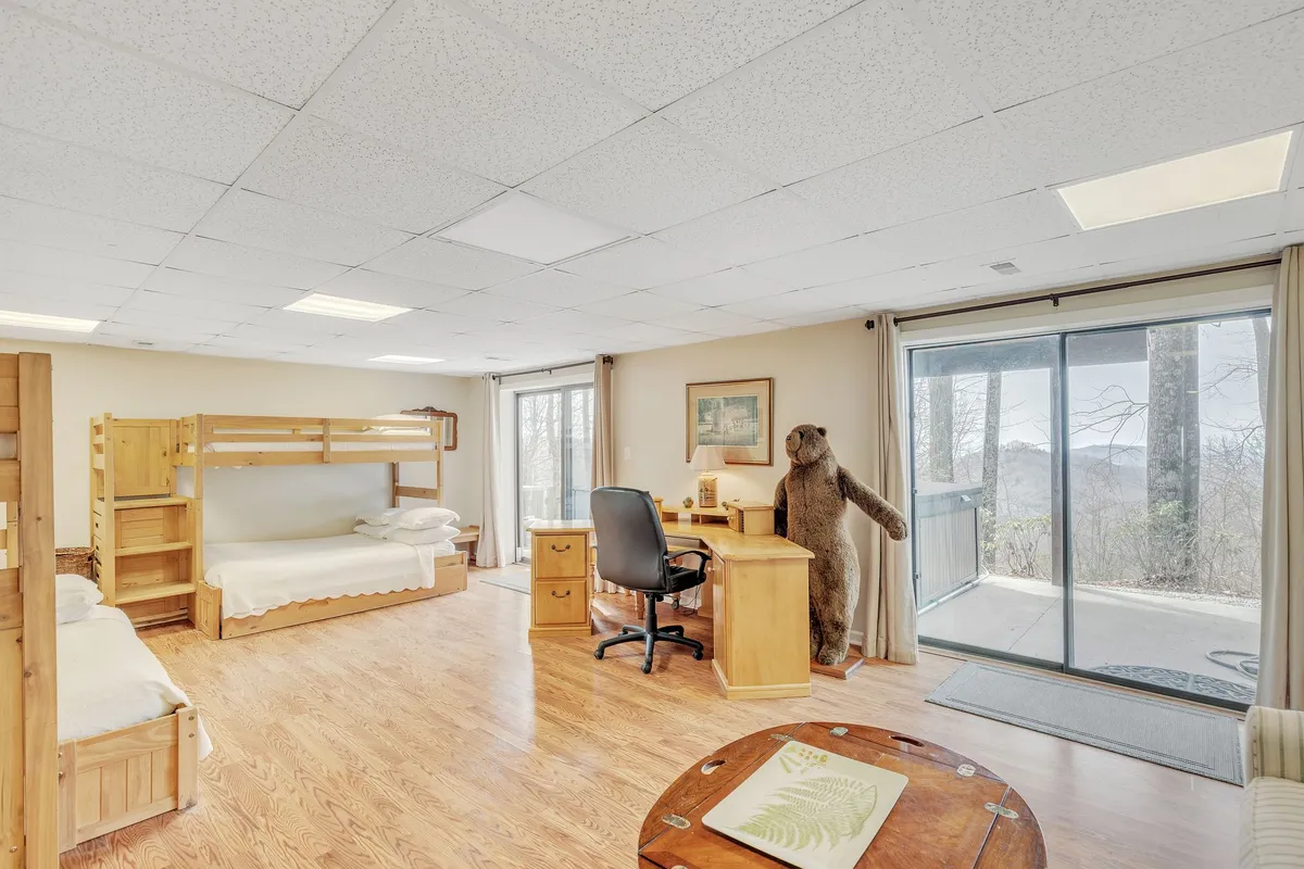 This interior photo captures a set of bunk beds, a desk with a chair, a stuffed bear, and a large sliding glass door offering plenty of natural light. The space feels comfortable and playful, making it perfect for children or extra guests to unwind, read, or play games.