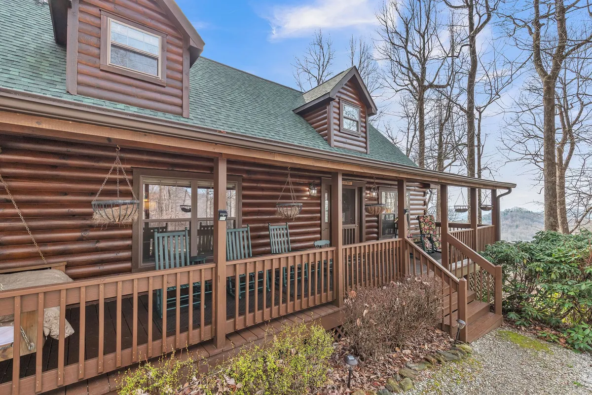 This exterior image shows the inviting log cabin structure, porch seating, and a sweeping landscape view. The setting is cozy, with the porch ideal for relaxing, soaking in mountain vistas, or gathering with loved ones as the sun sets.