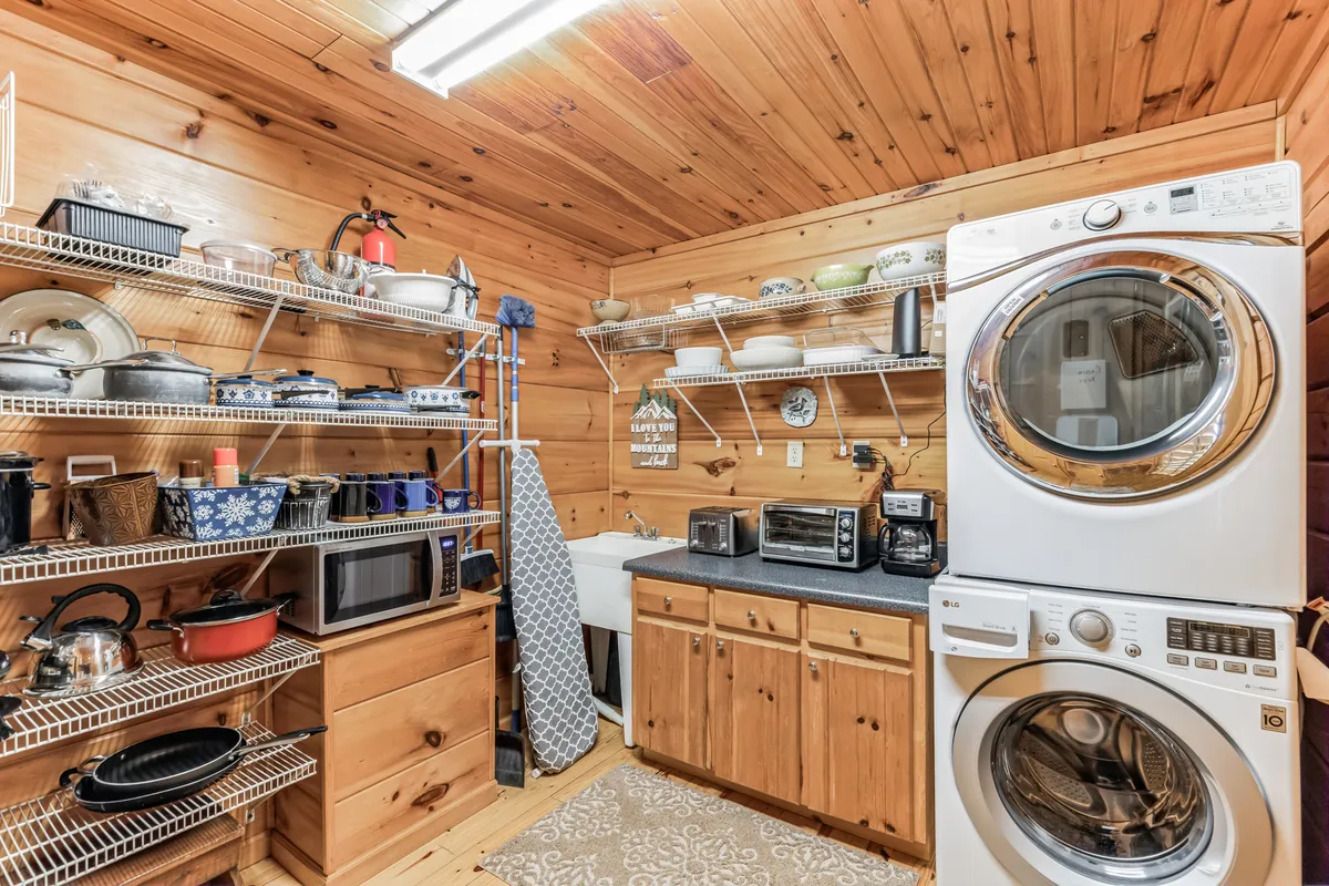 A practical pantry and utility area featuring shelves filled with cookware and kitchen supplies, as well as countertop appliances and wooden cabinetry. The scene is warm and functional, emphasizing ample storage and preparation space.